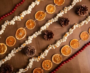 a string of dried oranges, pine cones, popcorn, and beads on a wooden table