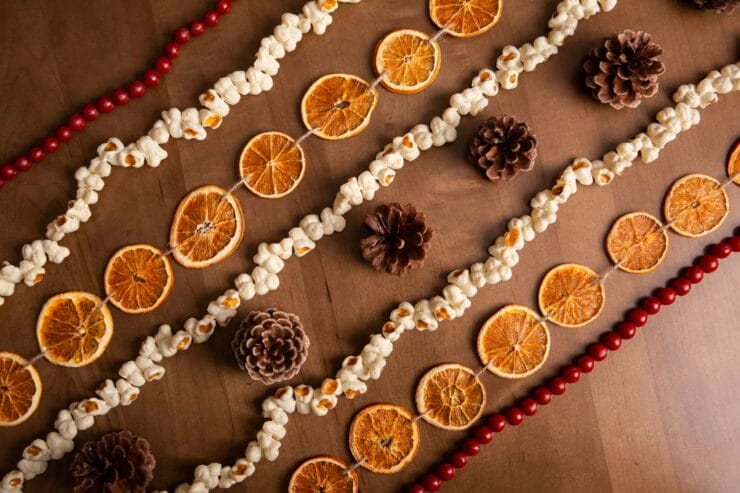 a string of dried oranges, pine cones, popcorn, and beads on a wooden table