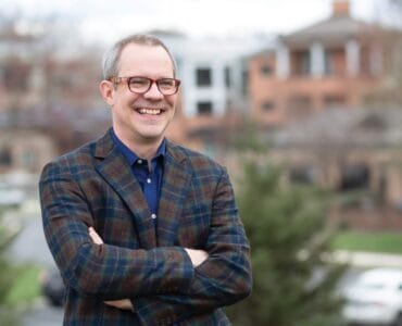 a man in a plaid suit and glasses is smiling with his arms crossed