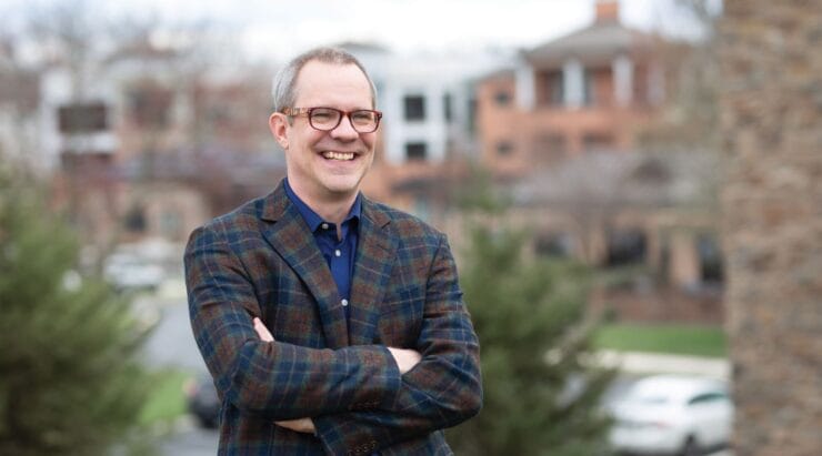 a man in a plaid suit and glasses is smiling with his arms crossed