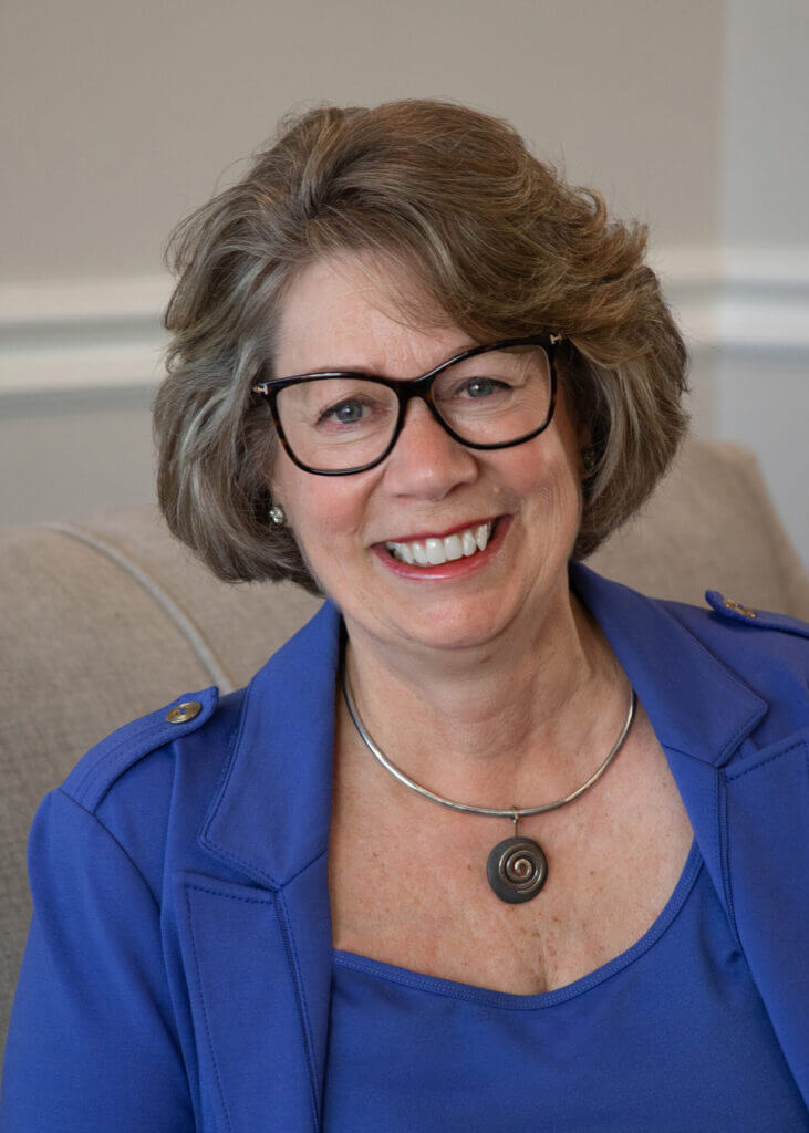 a woman wearing glasses and a blue jacket smiles for the camera