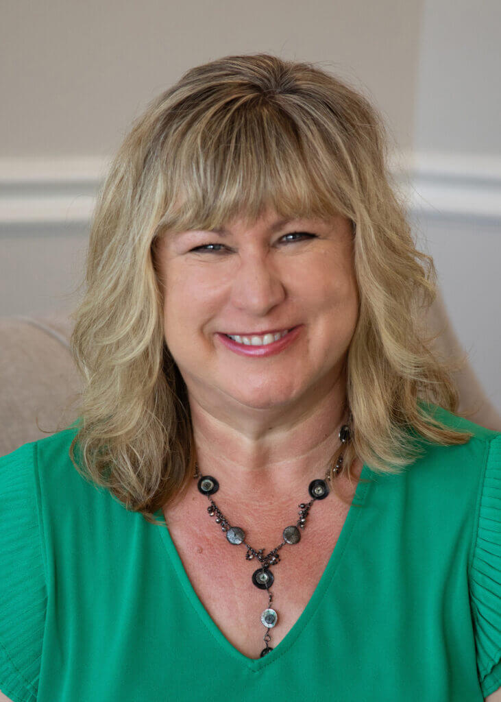 a woman wearing a green shirt and a necklace smiles for the camera