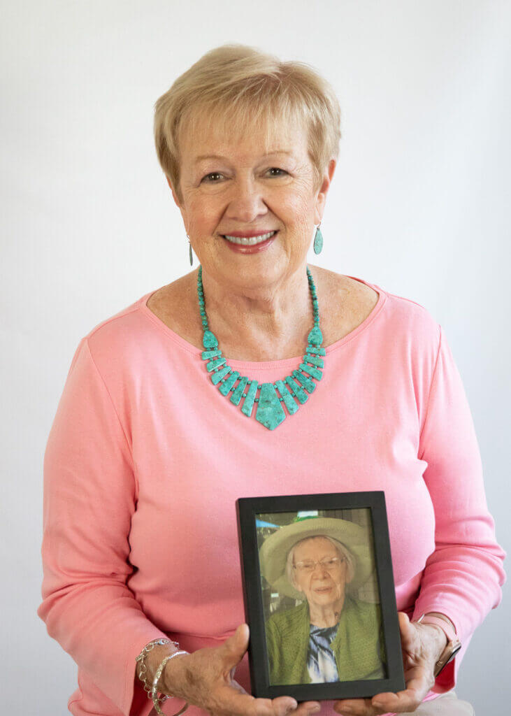 a woman in a pink shirt is holding a picture of her grandmother