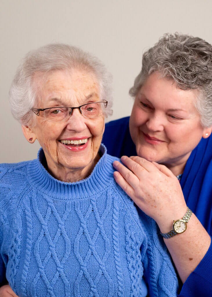 an elderly woman wearing glasses and a blue sweater is being comforted by a woman wearing a watch